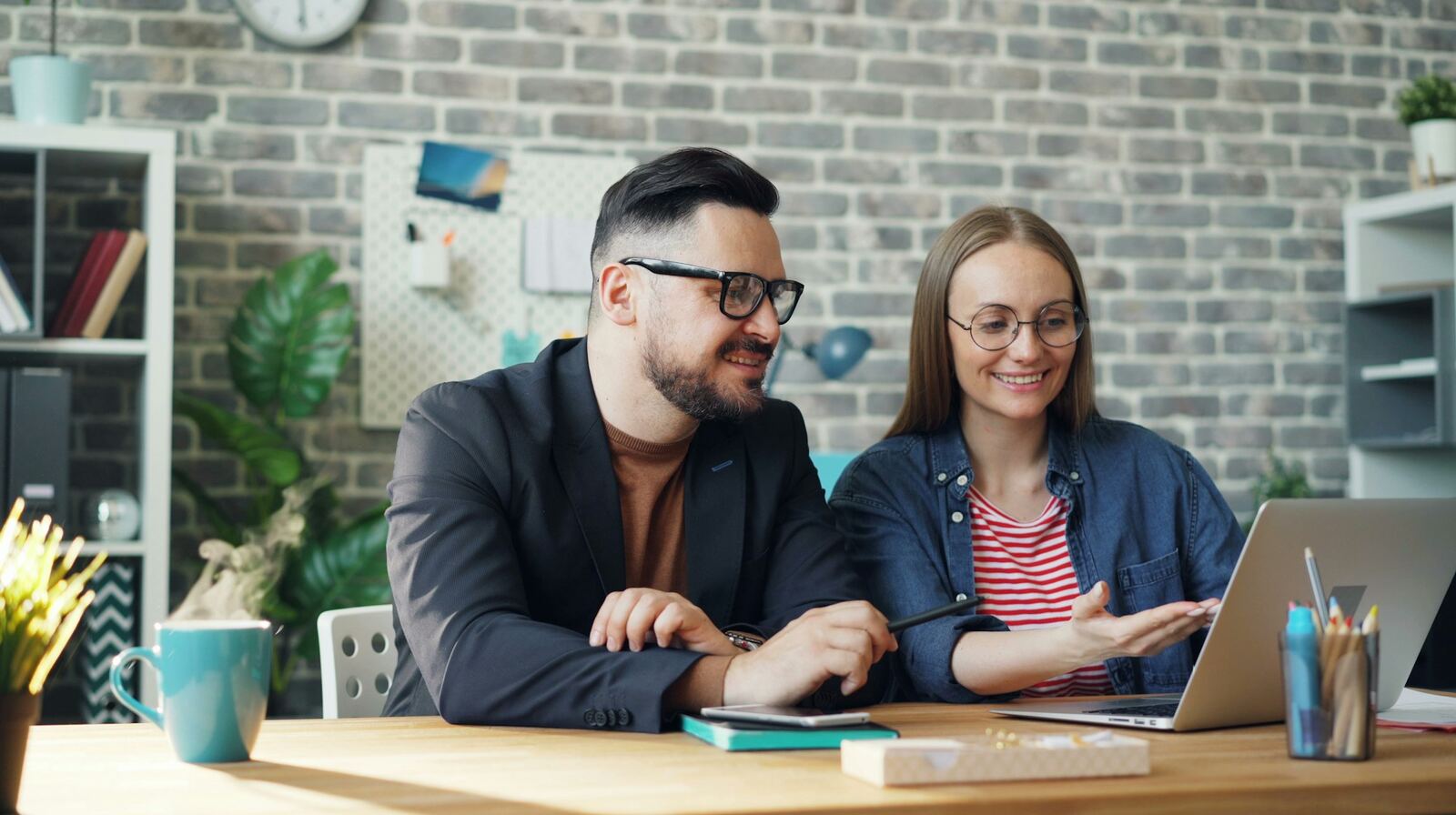Two colleagues working at a desk and looking at a laptop screen